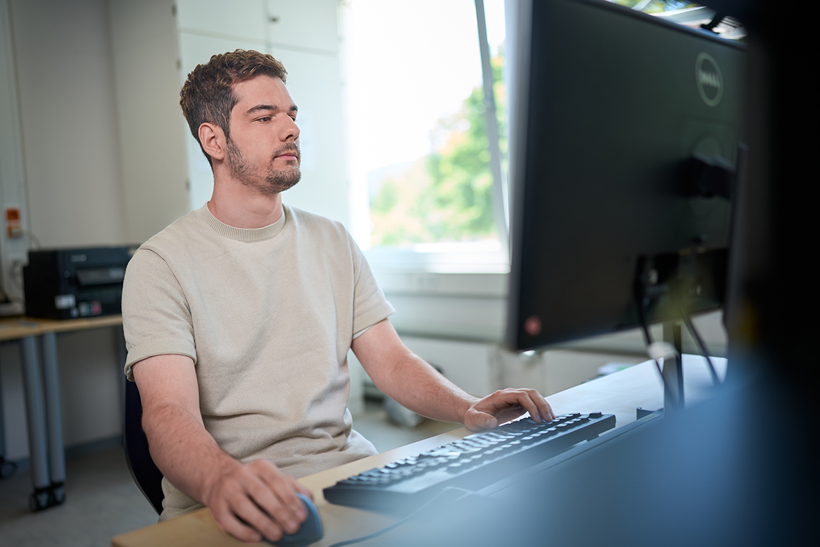 Das Bild zeigt einen Mann der vor einem Computer sitzt