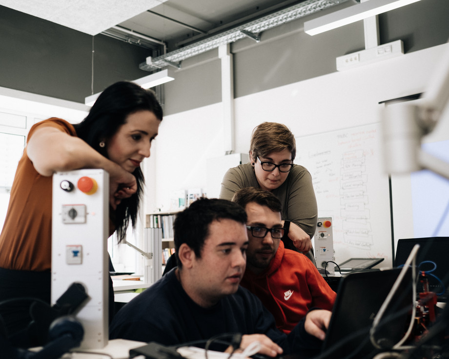 Drei junge Menschen schauen gespannt auf einen Laptop-Bildschirm und verfolgen aufmerksam, was darauf zu sehen ist.