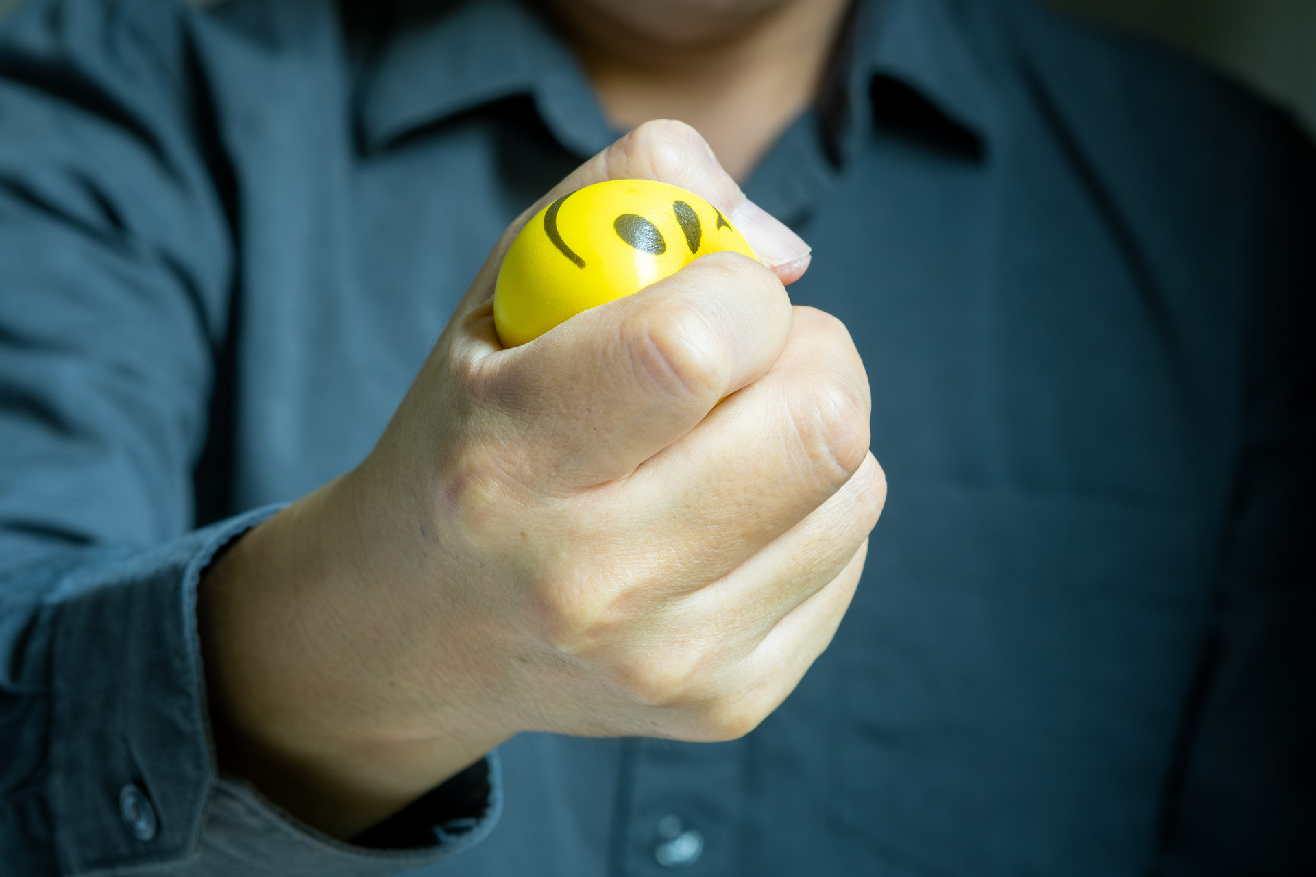 Person hält gelben Stressball mit Gesicht.
