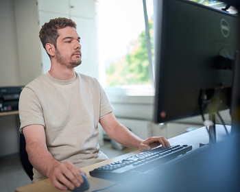 Das Bild zeigt einen Mann der vor einem Computer sitzt
