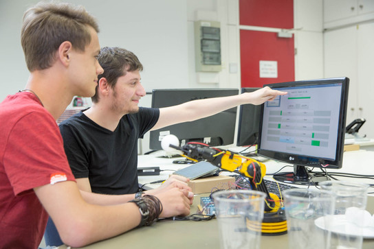 Zwei Auszubildende in der IT, programmieren Roboterarm