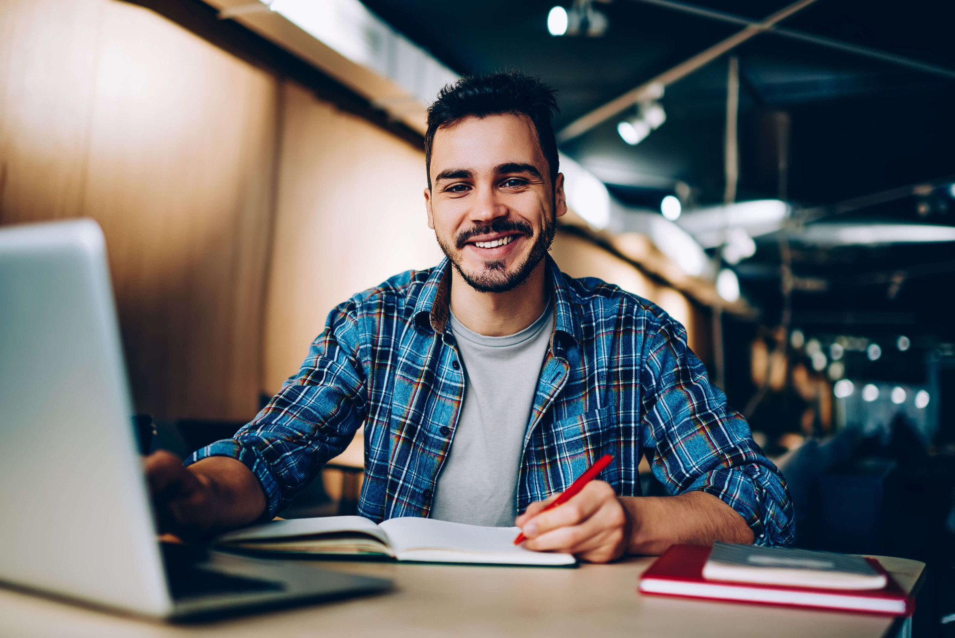 Lächelnder junger Mann sitzt an einem Laptop und schaut sich die Webseite des SRH Berufsbildungswerk Neckargemünd an.
