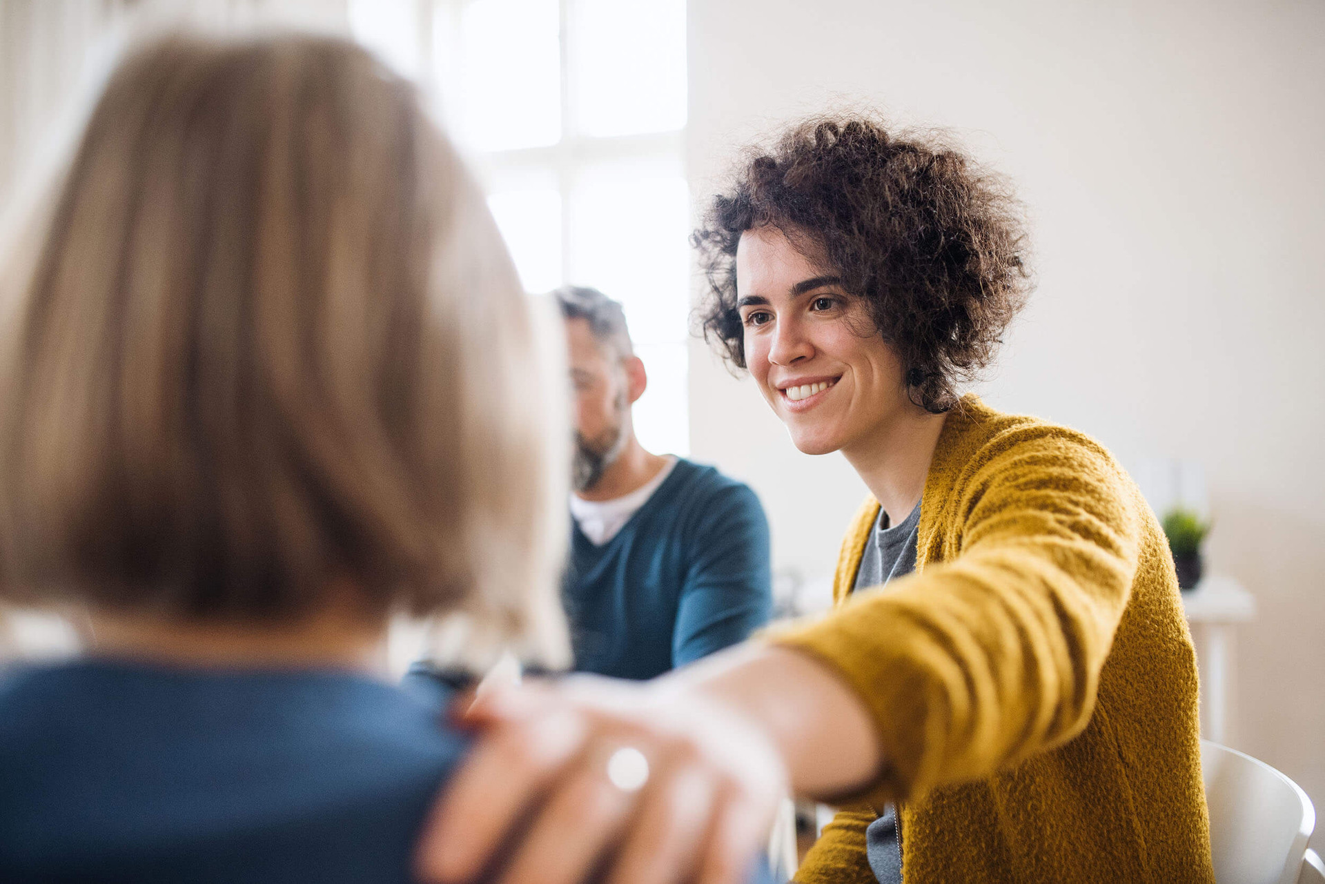 Drei Personen sitzen in einem Meeting, eine Person lächelt.