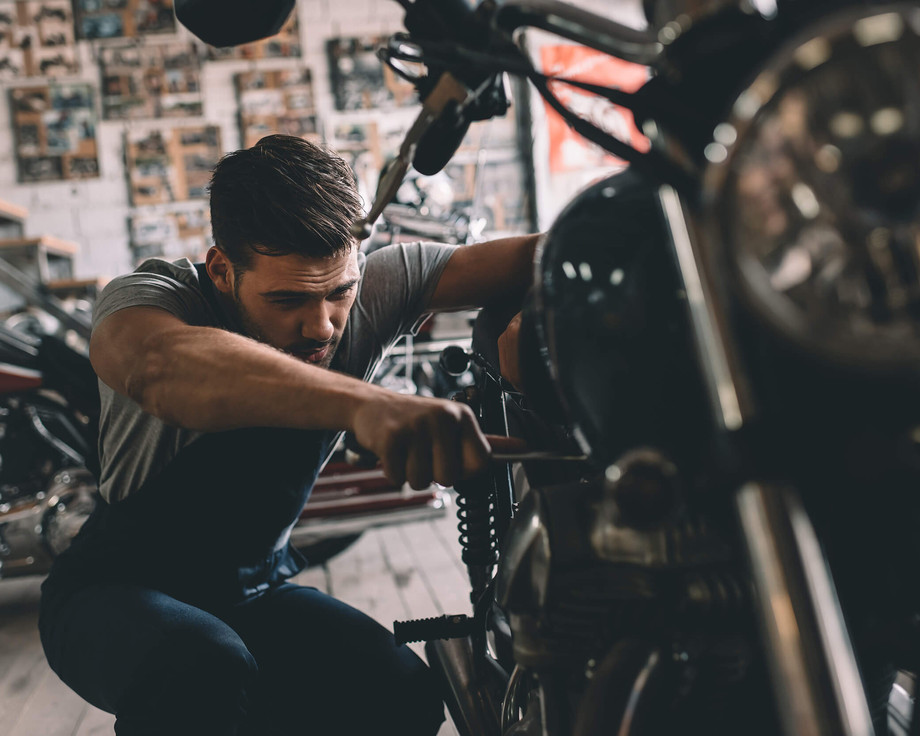 Ein junger Auszubildender zum Zweiradmechatroniker benutzt Werkzeug um ein Motorrad zu reparieren.