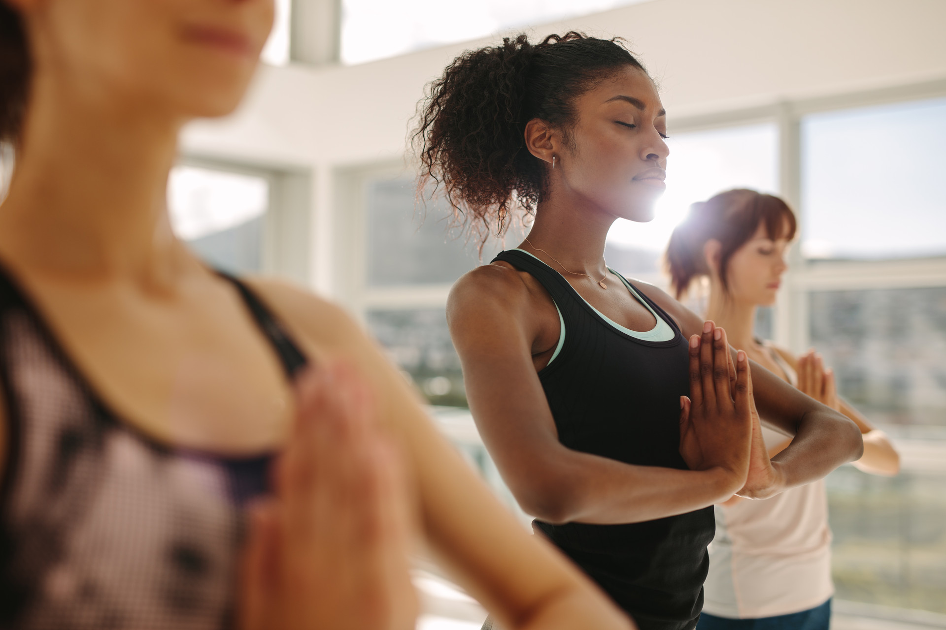 Drei Personen üben Yoga in einem hellen Raum.